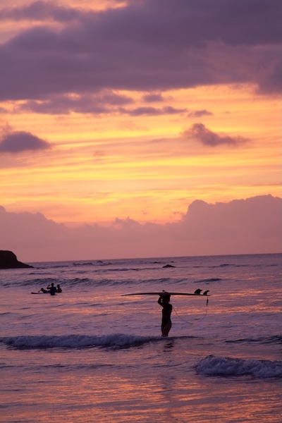 Mujer sosteniendo una tabla de surf en el agua al atardecer