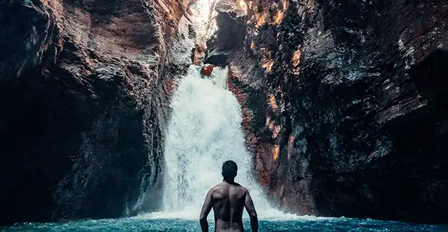 Un hombre de pie en el agua frente a una cascada.