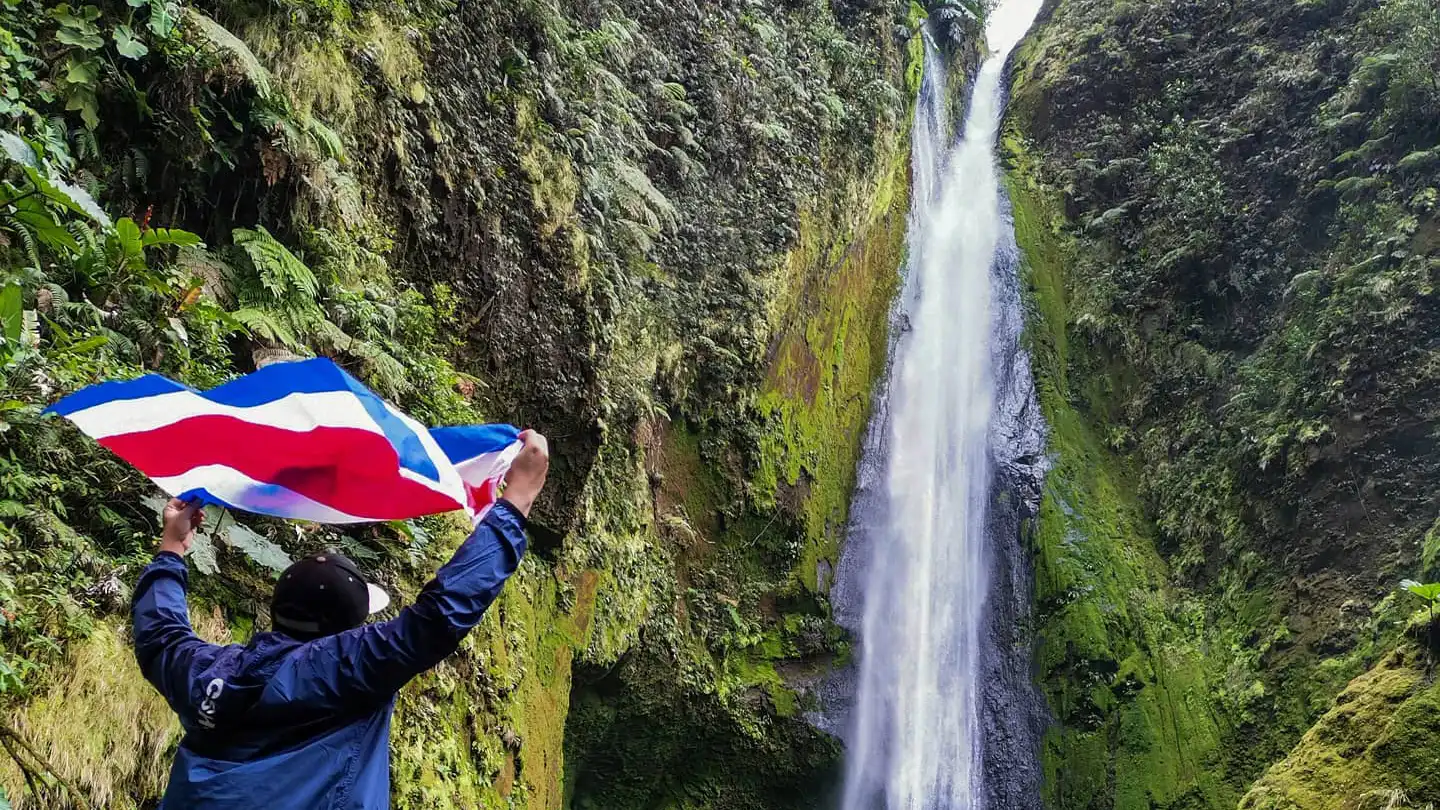 Un hombre sostiene una bandera frente a una cascada.