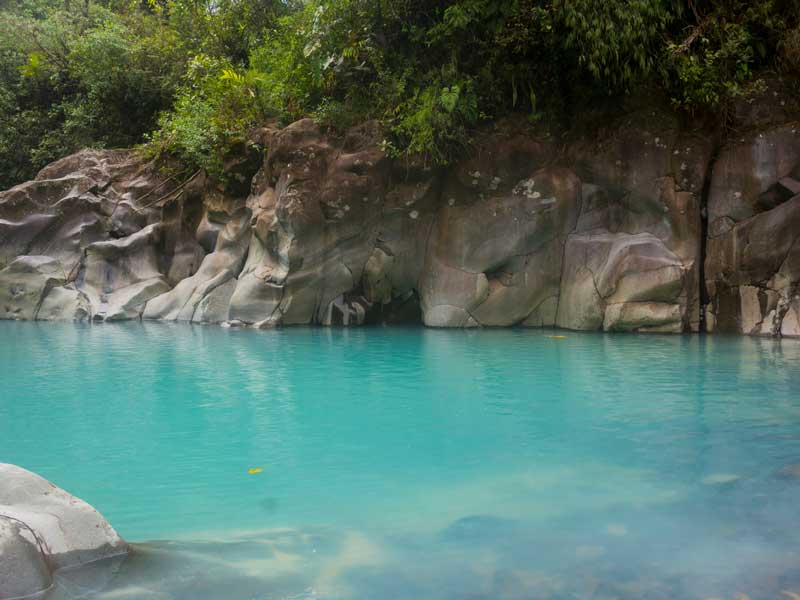 Un estanque de agua azul rodeado de rocas y árboles.