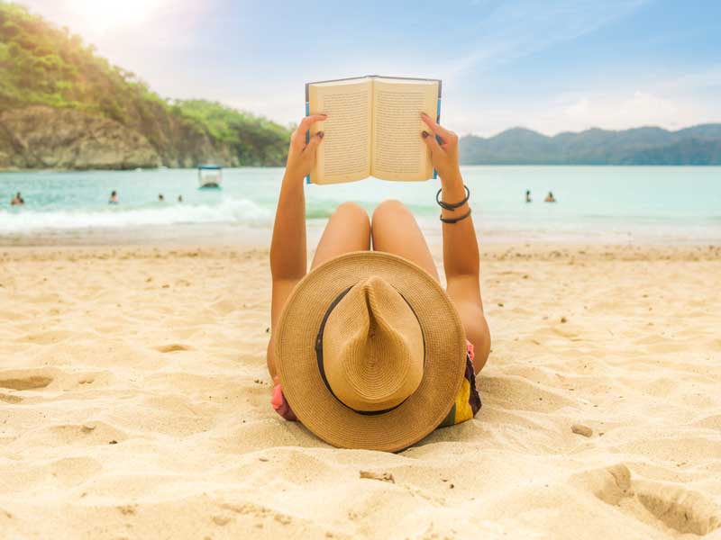 Una mujer tumbada en la playa leyendo un libro.