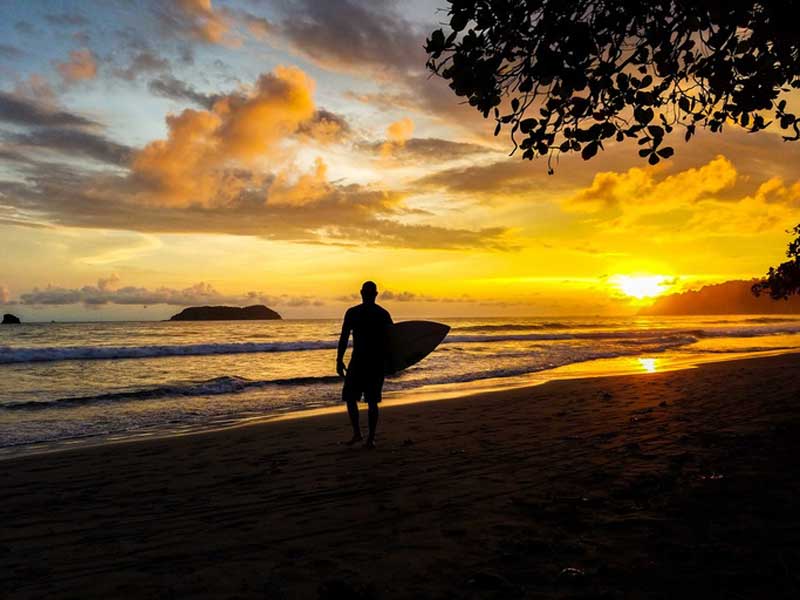 Un hombre sostiene una tabla de surf en una playa.