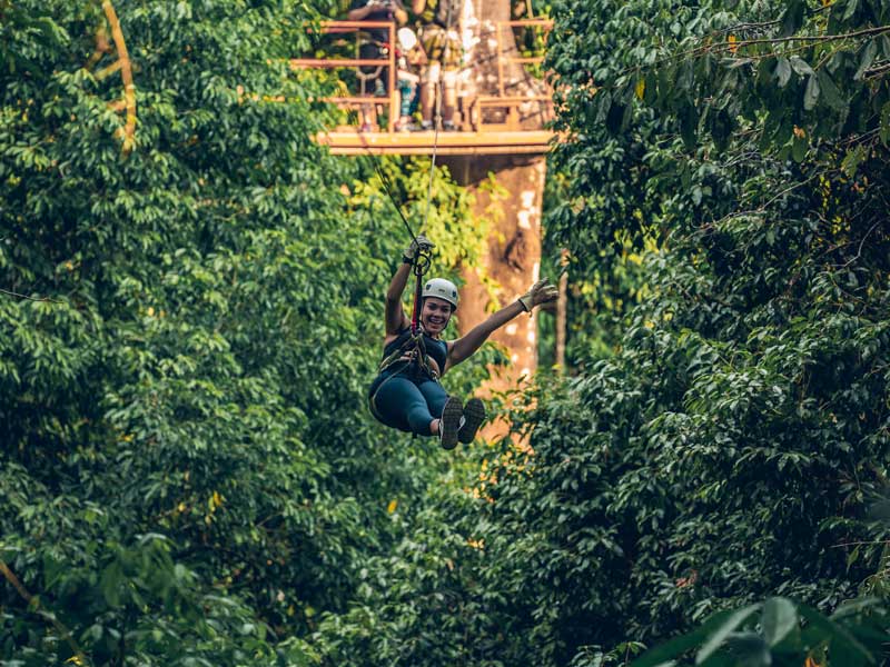 Una mujer montada en una tirolina en medio de un bosque.