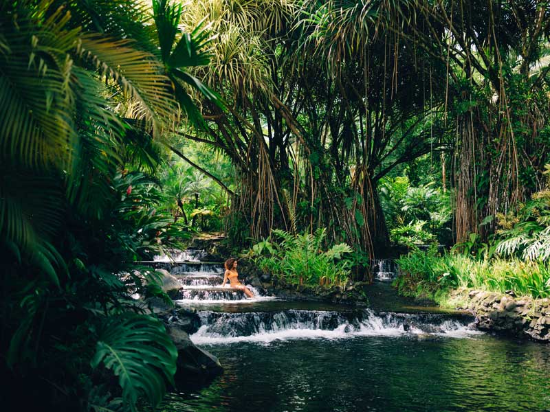 Una mujer está sentada en una pequeña cascada de la selva.
