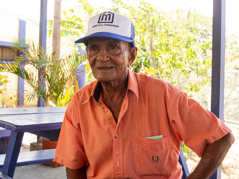 Un anciano con sombrero sentado en una mesa de picnic.