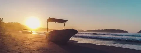 La vista de la puesta de sol y el mar, con el barco varado en la playa