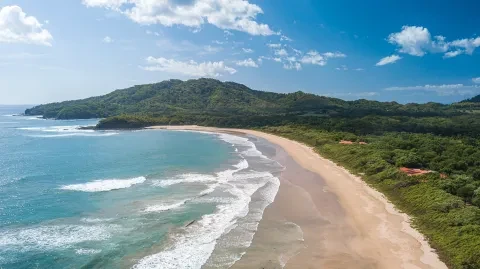Vista aérea de una playa de arena situada en la costa del Pacífico de l Costa Rica, rodeada de aguas turquesas y exuberantes colinas verdes.