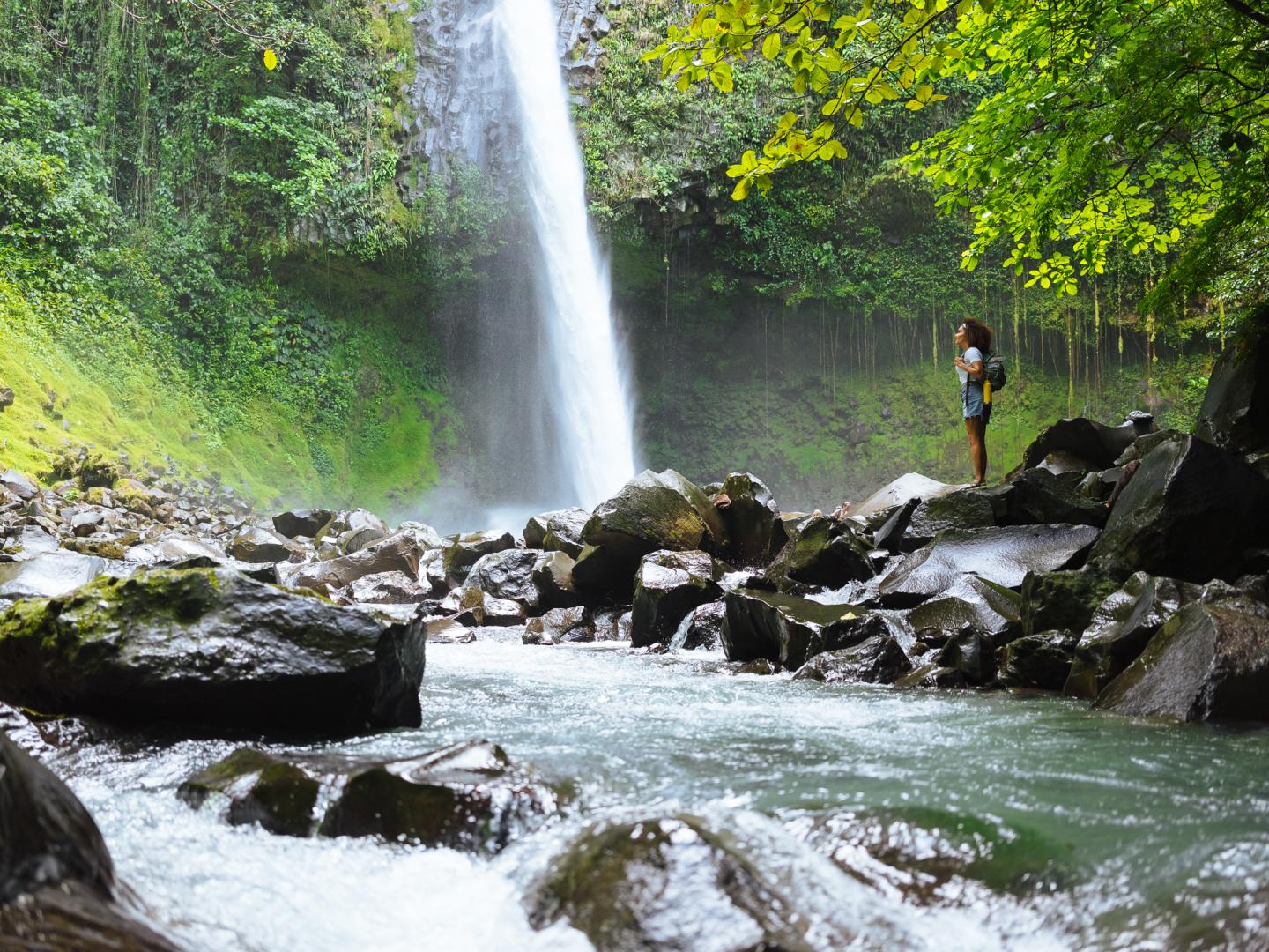 Mujer de pie junto a una cascada en la selva.