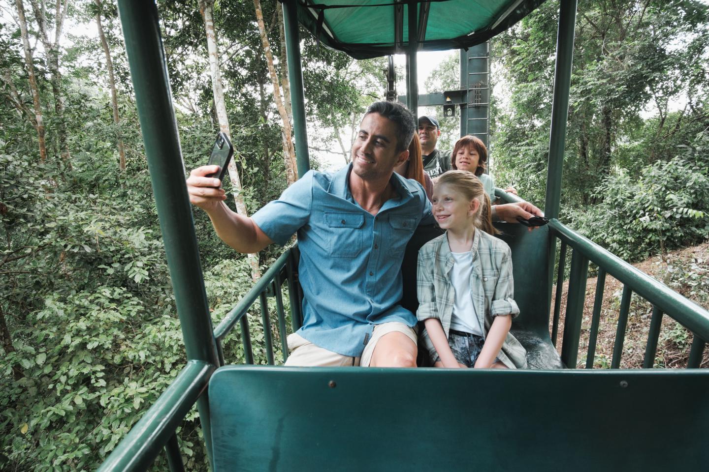 Una familia haciéndose un selfi en una góndola al aire libre sobre el dosel del bosque tropical.