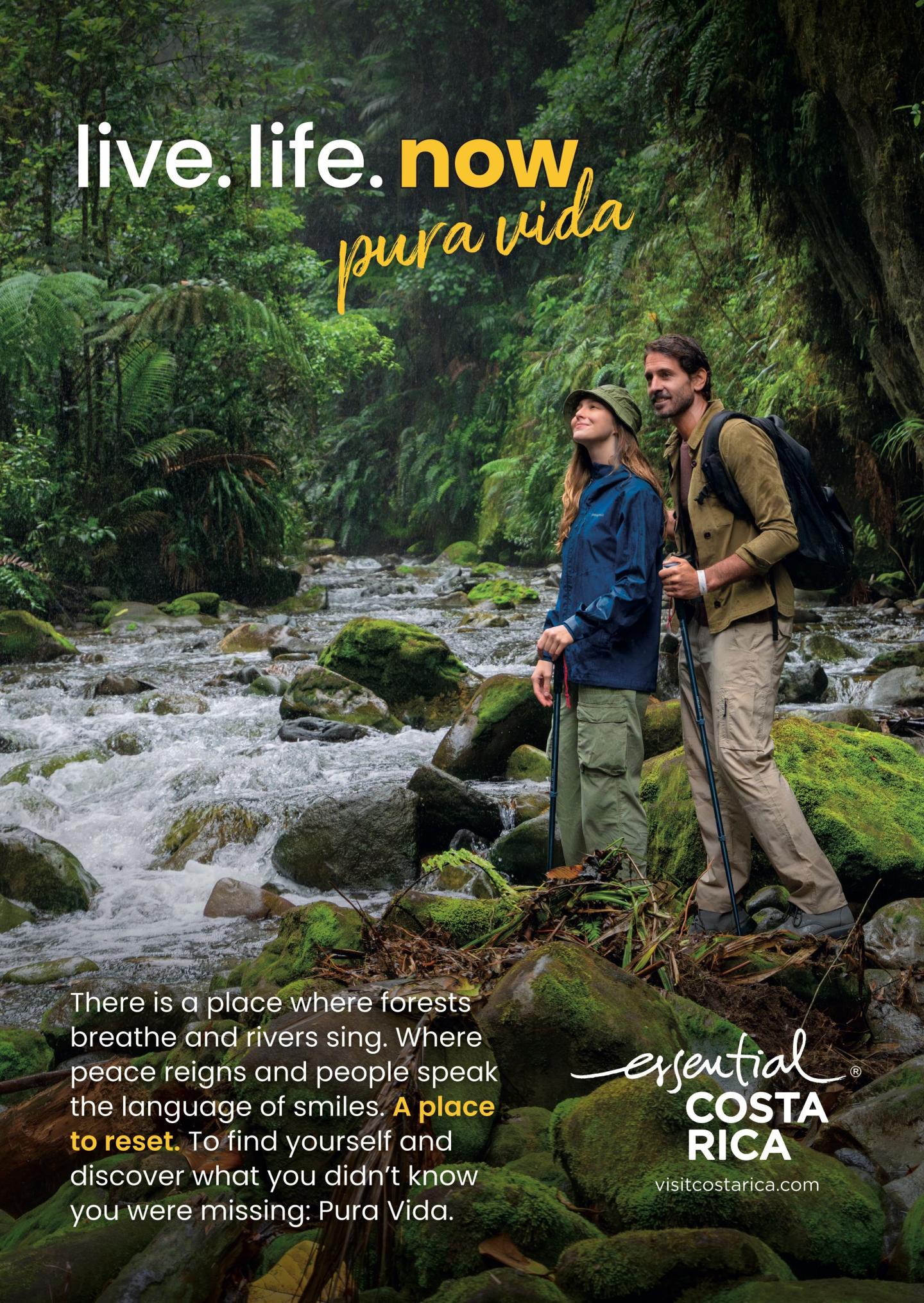 Anuncio en el que aparecen dos excursionistas de pie sobre rocas cubiertas de musgo junto a un río en una exuberante selva tropical. Titulares: «live.life.now» ypura vida». El texto describe bosques que respiran, ríos que cantan y la oportunidad de empezar de cero. Logotipo: «esencial Costa Rica, visitcostarica.com.