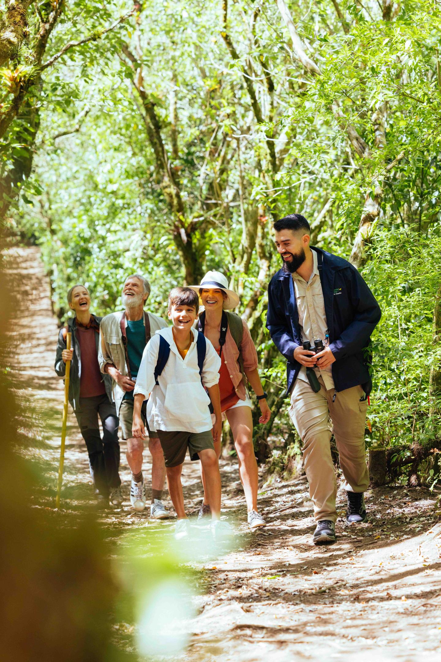 Un pequeño grupo de viajeros camina por un sendero boscoso a la sombra, acompañado por un guía.